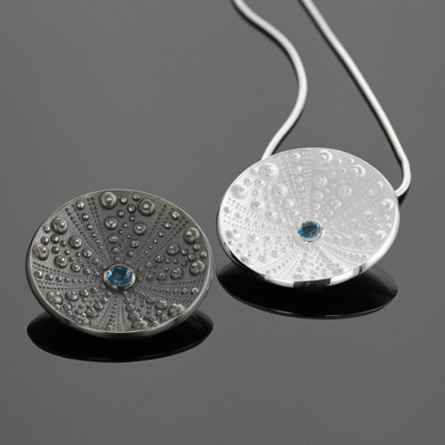 Disc shaped pendant in oxidised sterling silver with sea urchin patterns and a Blue Topas