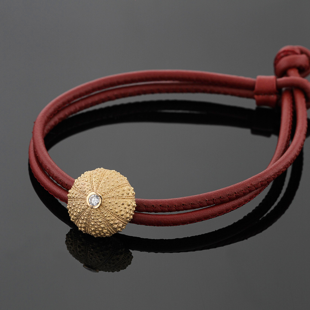 Sea urchin element in gold with a diamond put onto a red leather bracelet